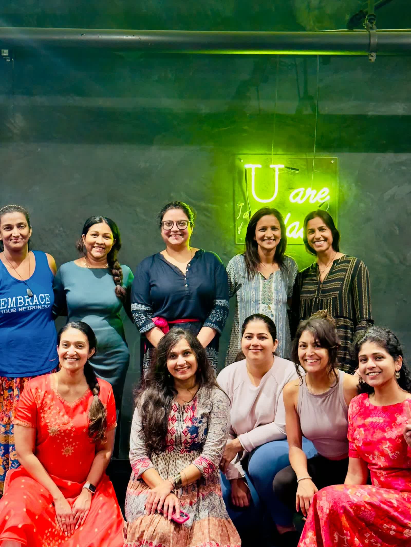 Group portrait of a workshop cohort seated and standing beneath a neon sign in the studio.