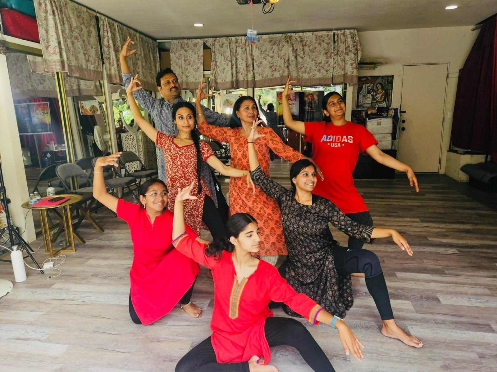 Class group in red and printed kurtas holding a layered Odissi pose together across the studio floor.