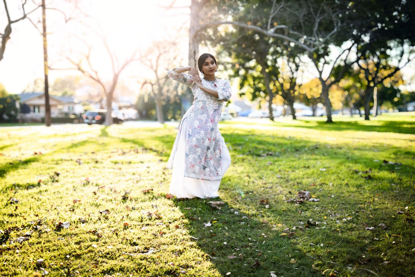 Wide shot of Yaman dancing in a sunlit park in a floral kurta and white skirt.