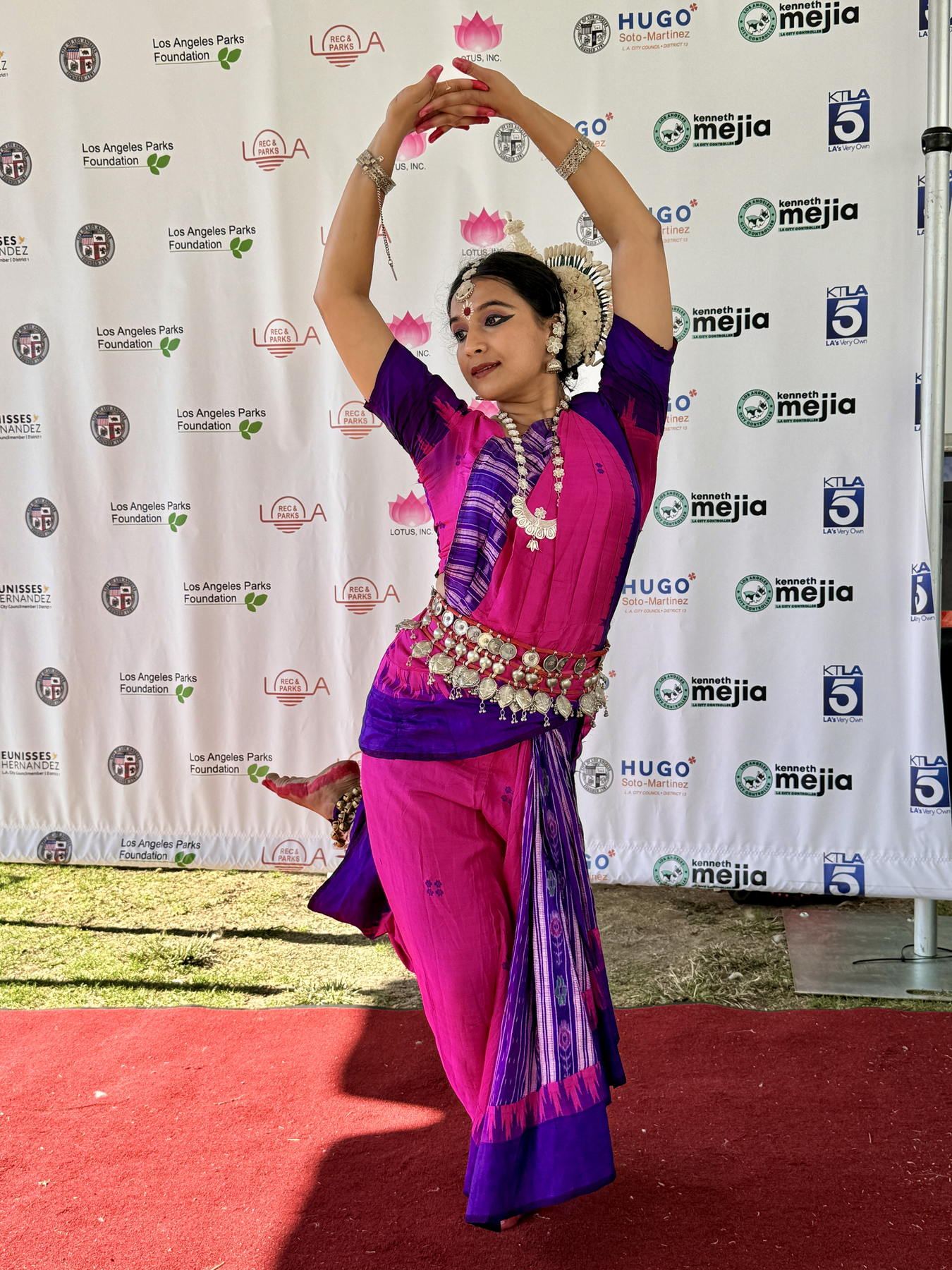 Yaman in a pink and purple Odissi costume, arms arched overhead, on the Lotus Festival stage in Los Angeles.