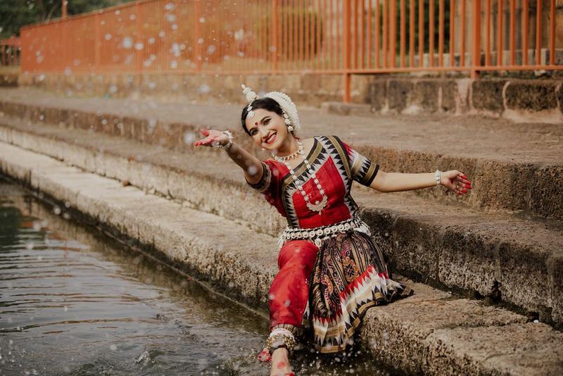 Seated on stone steps beside a temple tank, one arm sweeping across water, droplets caught in the air.