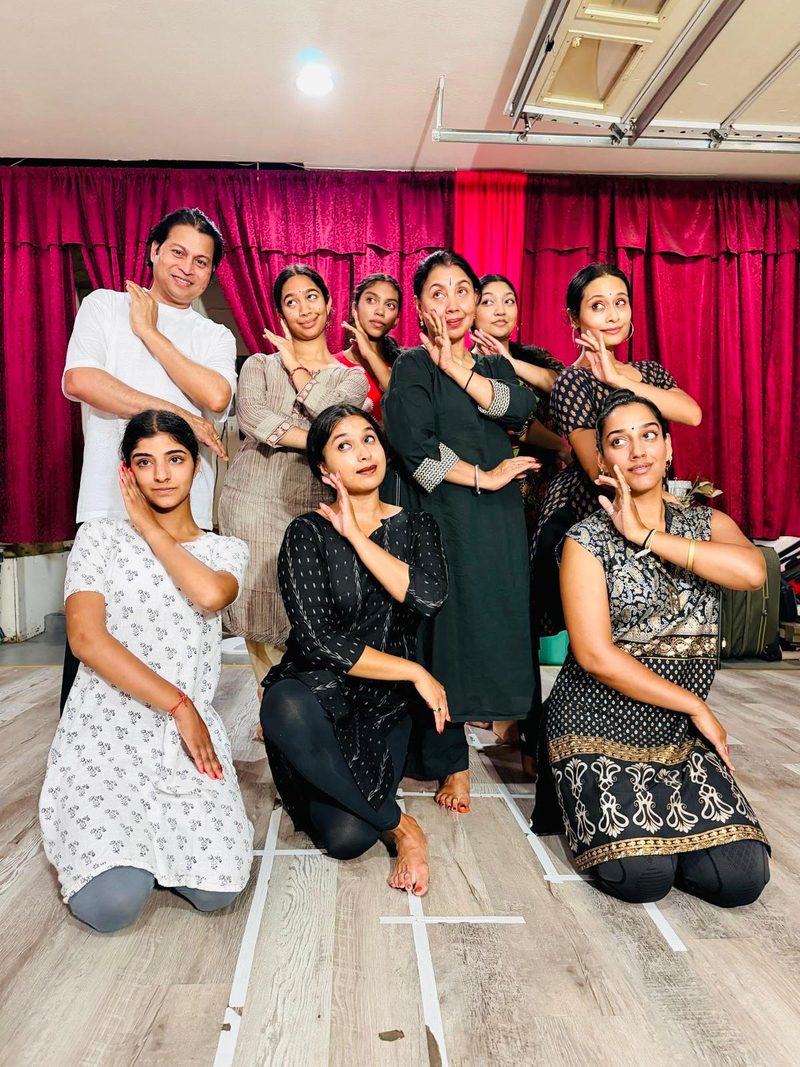 Workshop group holding a hand mudra together in front of a deep red curtain backdrop in the studio.