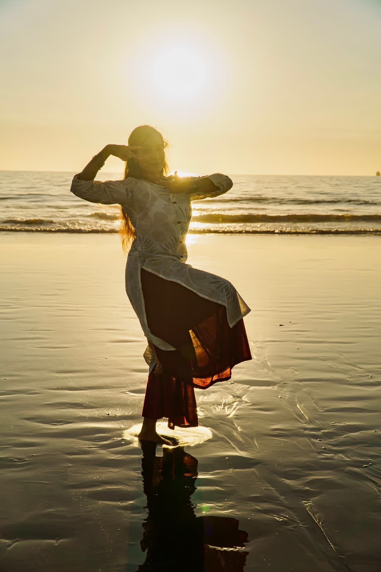 Silhouette of a dancer on a beach at sunset, arms framing the sun.